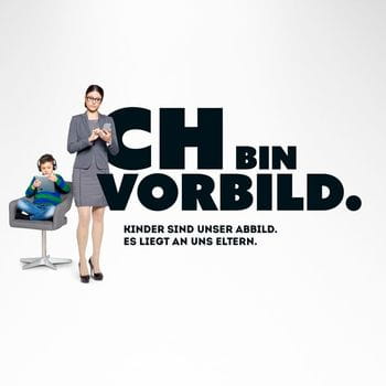 negatives Sujetbild zur Kampagne Ich bin Vorbild zeigt eine Mutter, die mit ihrem Handy beschäftigt ist, der Sohn sitzt nebenbei auf einem Bürostuhl und ist mit einem Tablet beschäftigt