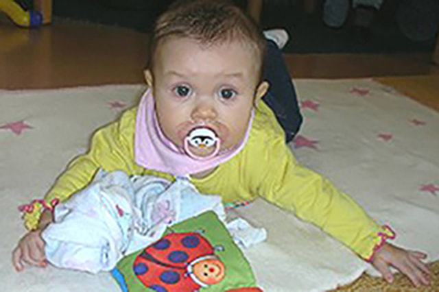 Baby mit Schnuller am Bauch liegend